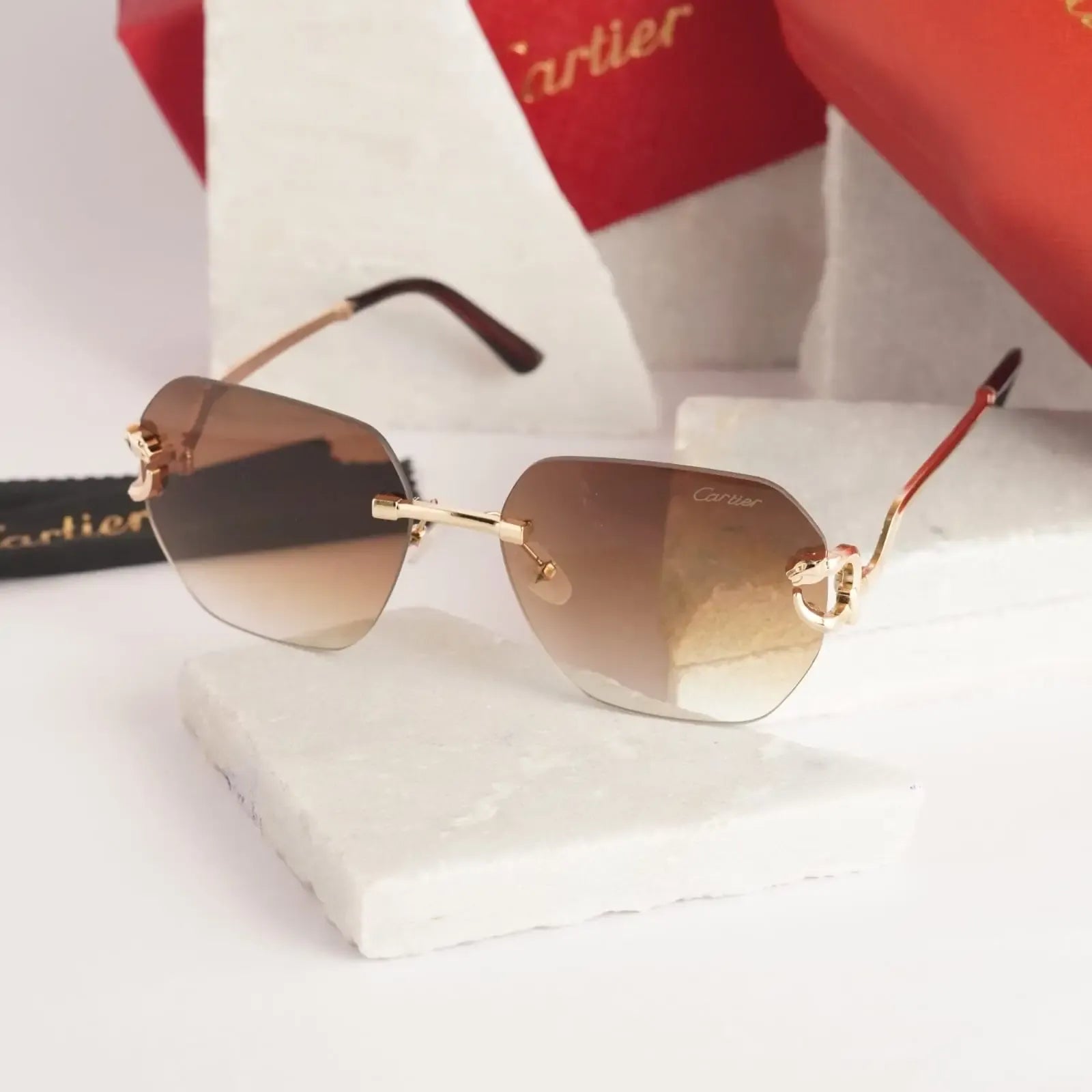 Rimless gold panther brown gradient sunglasses - flat lay with Cartier cleaning cloth on marble