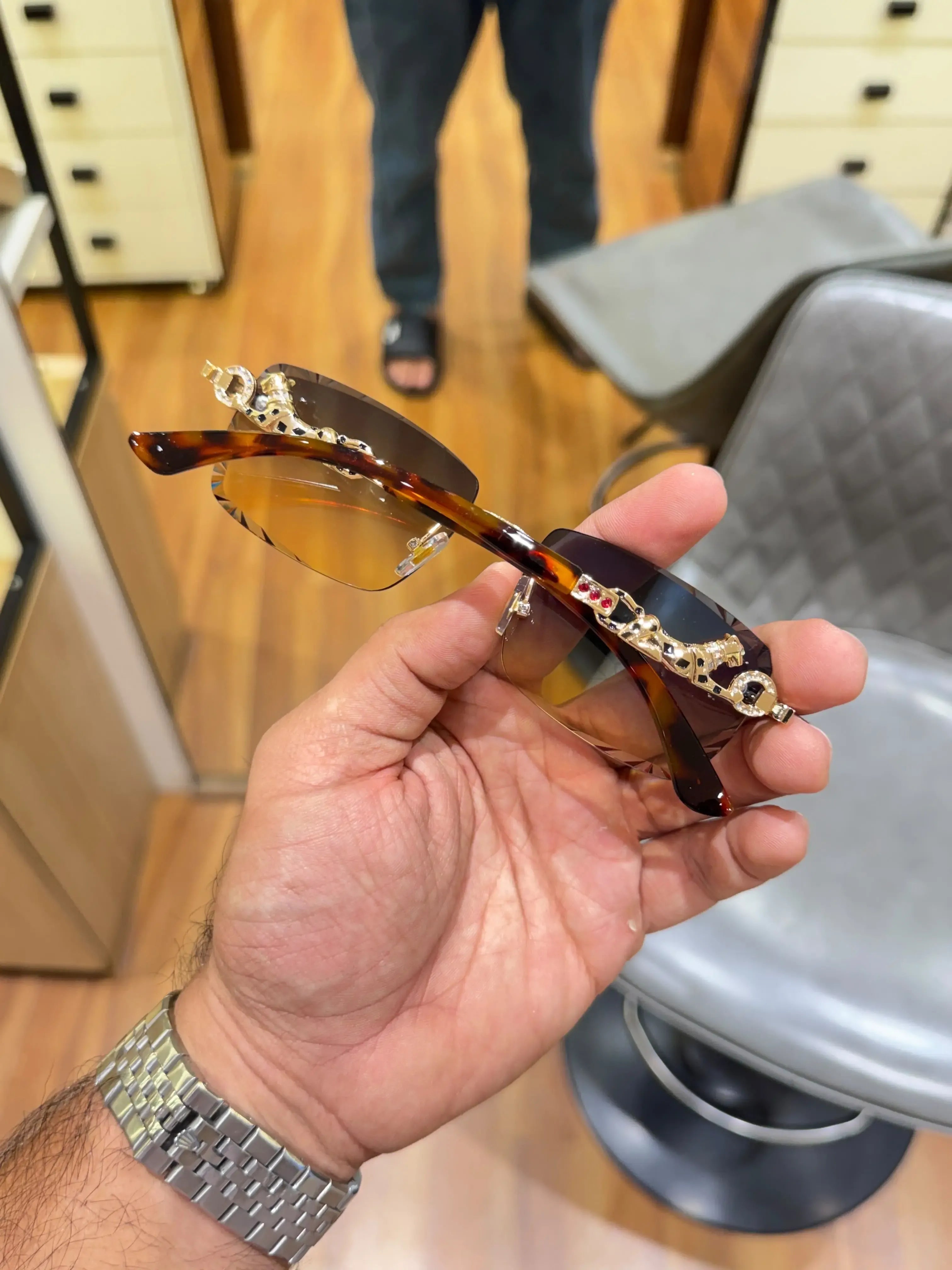Rimless gold panther sea green sunglasses - held in hand showing tortoise temples and full panther body bridge detail