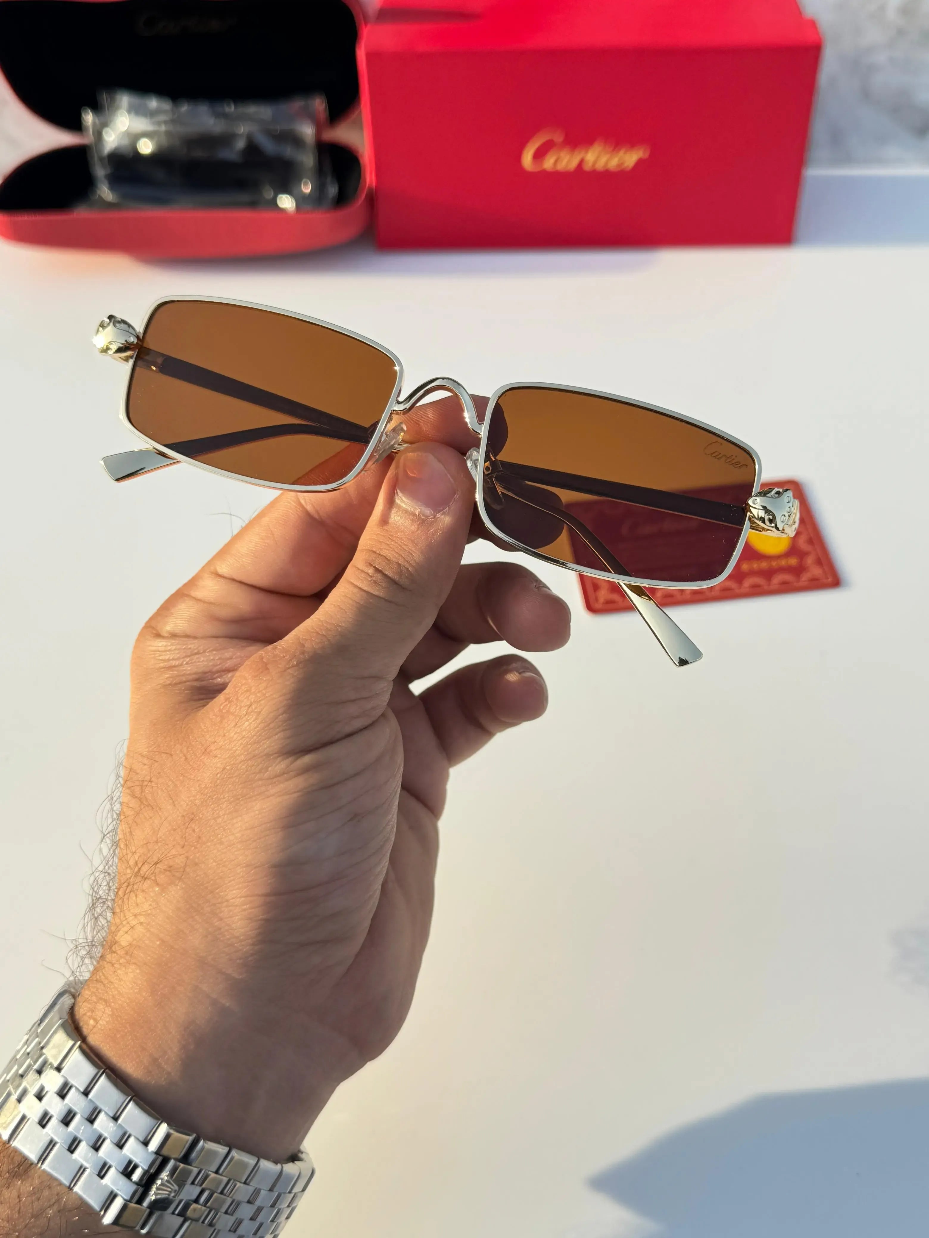 Gold rectangular sunglasses with brown lenses - held in hand showing full frame front view