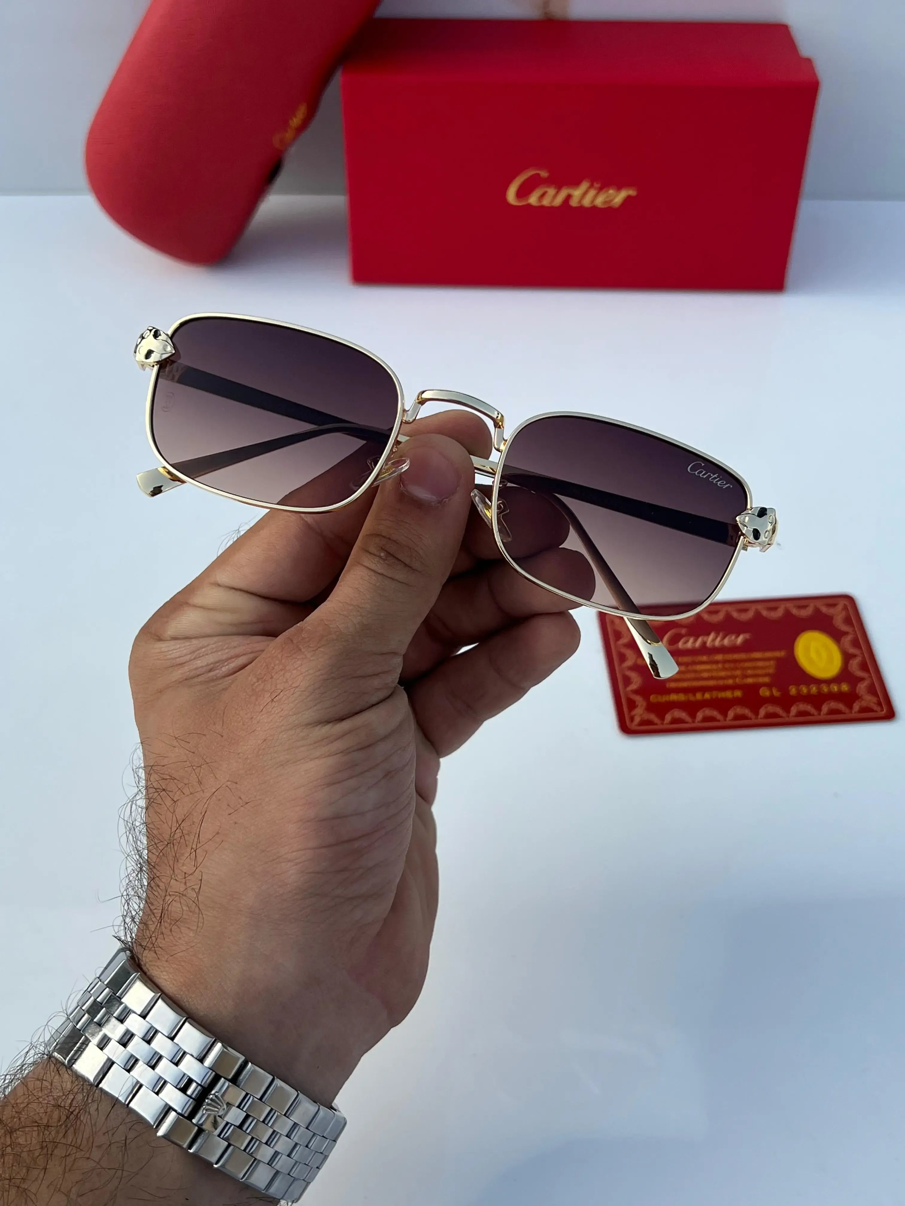 Gold rectangular sunglasses with brown gradient lenses - held in hand showing full frame front view with Cartier card