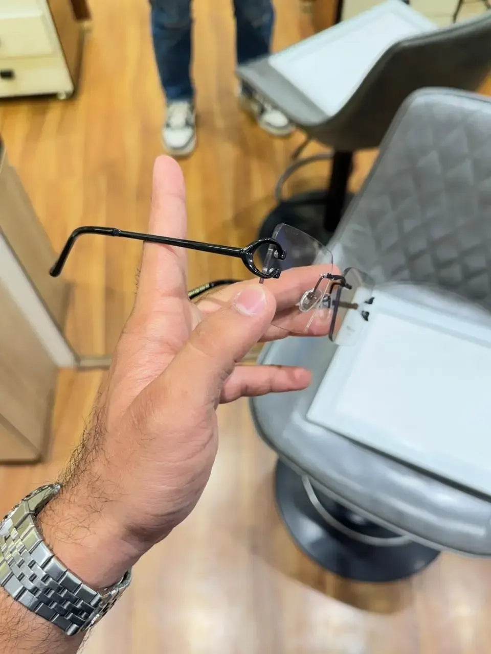 Rimless black C-frame eyeglasses - held showing C-shaped end piece detail