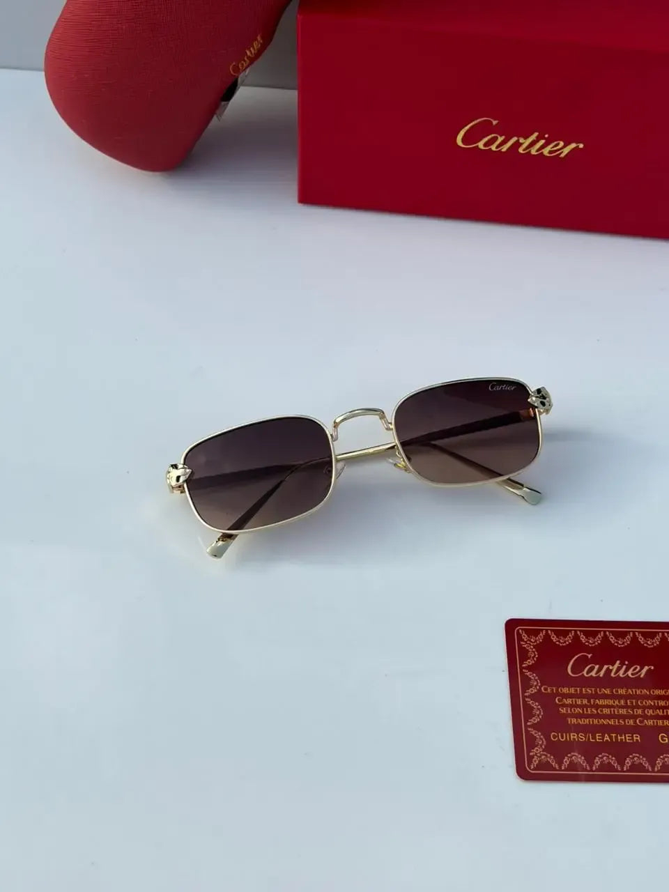 Gold rectangular sunglasses with brown gradient lenses - held in hand showing 3/4 angle with panther hinge detail